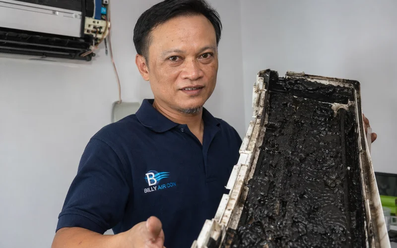 Technician holding aircon drain pan caked with sludge